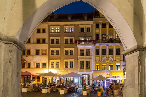 View through the arches of the arcades of the hall houses to the row of street cafés at night,