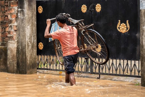 A person carries a bicycle as he wade through a flooded street after heavy rains in Guwahati, India