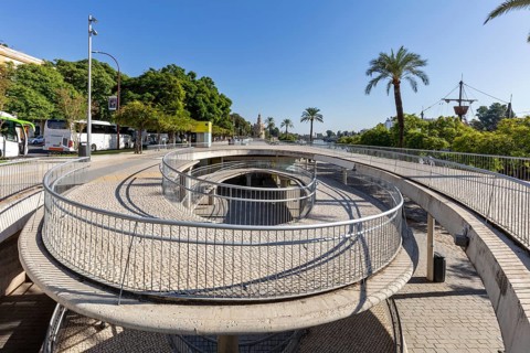 Modern pedestrian bridge with circular paths and palm trees in sunny weather, Seville