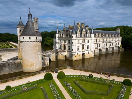 Frontal view of an imposing castle on the river Cher with manicured gardens and dramatic cloudy