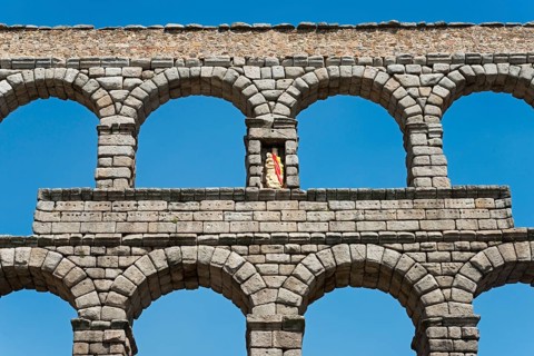 Close-up of a stone aqueduct with several arches under a clear blue sky in Segovia, Aqueduct,