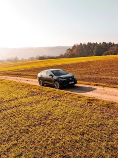 A car drives alone on a country lane, surrounded by golden fields under the sun, electric car VW