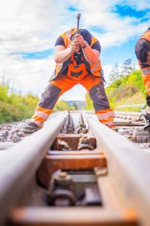 Two construction workers working on the rails, looking along the tracks in a rural setting, rail
