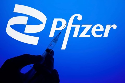 A gloved hand holding a syringe in front of the pfizer logo. Pfizer Inc. is an American
