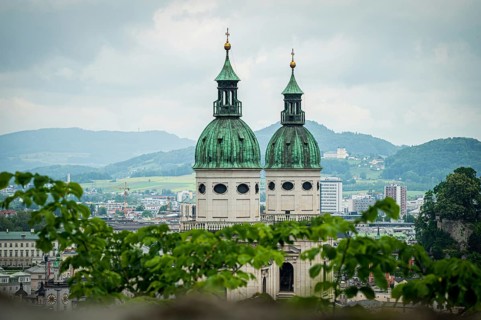 Two church towers with green roofs, framed by leaves, landscape in the background, Salzburg,