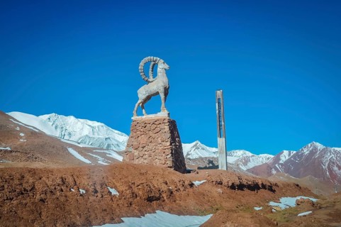 Sculpture of bouquetin on stony base surrounded by mountains with snowy peaks in distance in