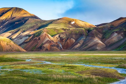 Green Valley is flooded with melt water. Snow lies in the hollows of colorful rhyolite mountains.
