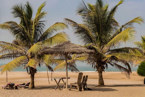 Two chairs and coffee table under a palm leaf and wood parasol on Bijilo Beach in The Gambia