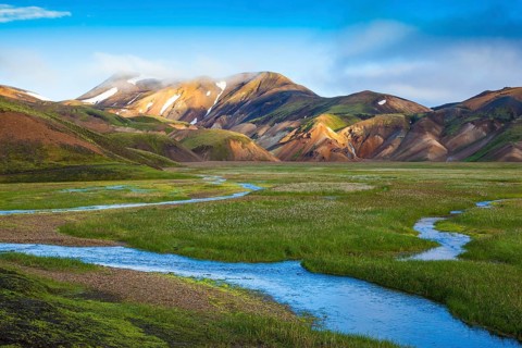 Snow lies in the hollows of colorful rhyolite mountains. Green Valley is flooded with melt water.