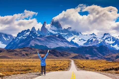 Woman delighted natural beauty raised her hands. The highway leads to the snow-capped peaks of