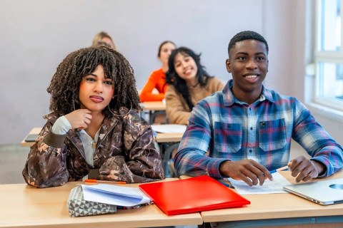 Multi ethnic students sitting at desks in a classroom, engaging with the teacher and absorbing