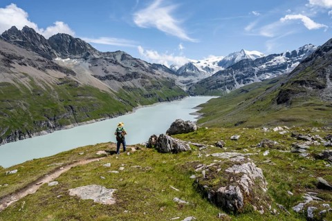 Mountaineer on a hiking trail at a blue mountain lake, reservoir Lac des Dix, behind mountain peak