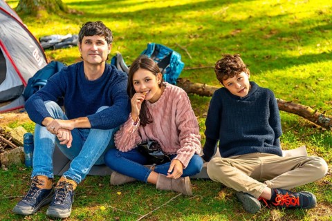 Happy caucasian father, daughter and son sitting next to camping tent enjoying nature in the forest