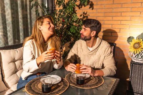 Smiling man and woman sharing a meal of burgers and drinks, creating a warm and intimate atmosphere