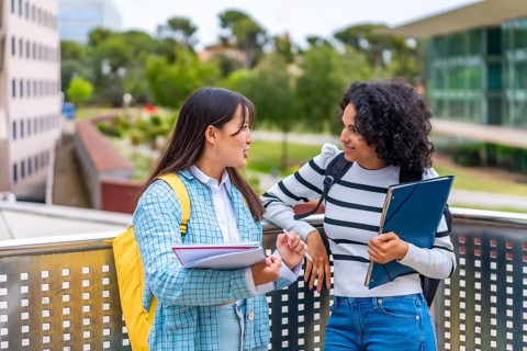 Two multi-ethnic female students reading and commenting notes standing outside the campus