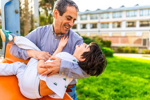 Grandfather holding and playing with his grandson at the playground, they are laughing and having