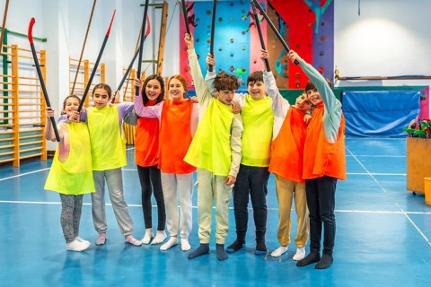 Group of cheerful students wearing colorful bibs raising hockey sticks and celebrating in school