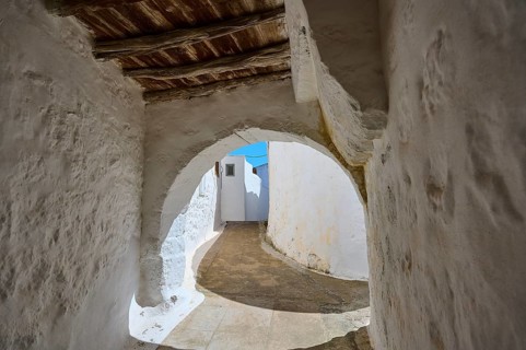 Arched passageway with wooden ceiling and white walls in a historic building, Chora, main town of