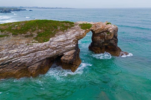 Rocky arch on the coast above the roaring ocean with green-blue water, aerial view, Praia das