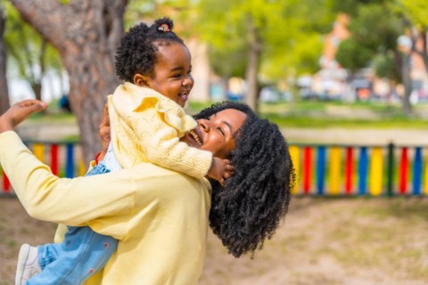 Joyful mother and adorable african girl embracing playing on a park