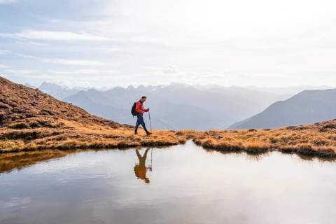 Mountaineer hiking with poles, reflected in a small mountain lake on the Krahberg, mountain