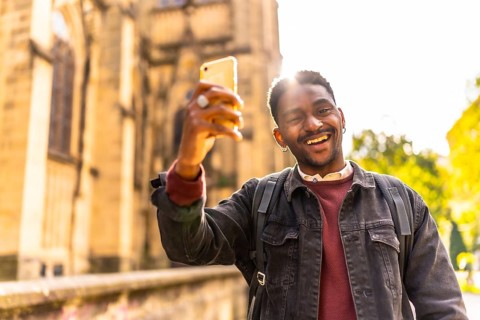 Happy and smiling african man enjoying walking along the city taking photos relaxed