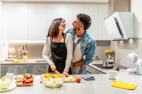 Young loving couple wearing aprons, preparing a healthy salad together in their modern kitchen,