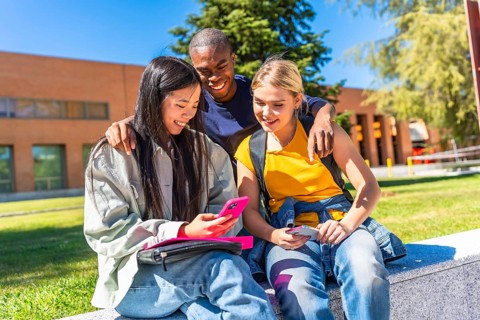 Happy mulit-ethnic group of exchange students using mobile outside the campus