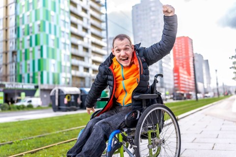 Happy disabled man celebrating raising his fist while sitting in a wheelchair in a city street
