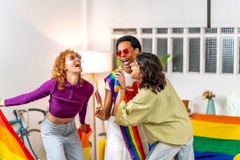 Multi-ethnic gay friends singing karaoke with toy mic celebrating pride at home