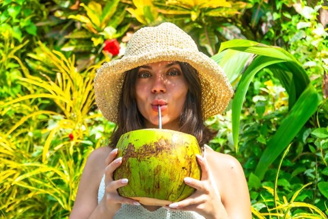 Young woman with straw hat savoring refreshing coconut water, surrounded by vibrant tropical