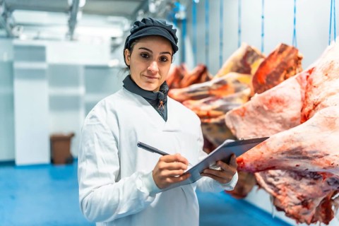 Female butcher making quality report writing notes in a clipboard in meat processing factory