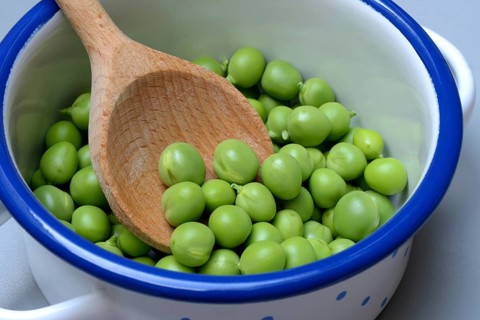 Fresh green peas in pot with wooden spoon, Pisum sativum