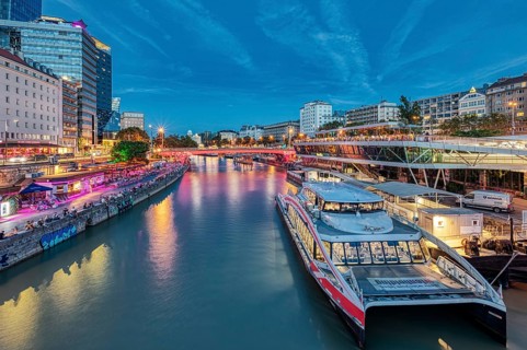 River scene with boats and illuminated city façade under a blue evening sky, Vienna