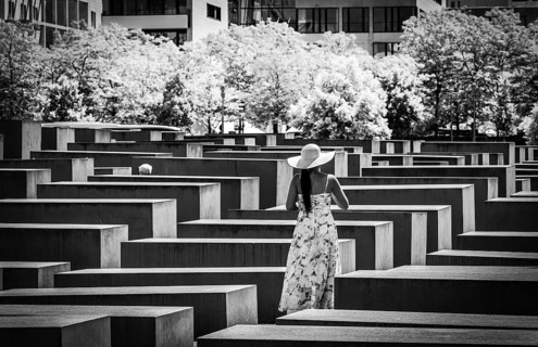 Black and white photograph, woman in summer dress amidst the Holocaust memorial steles at the