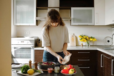 A woman is about to put fresh hake fillet on vegetables and bake the dish in the oven