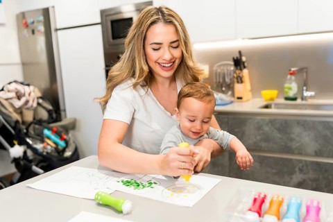 Happy mother and baby enjoying creative time, painting together in a bright, modern kitchen
