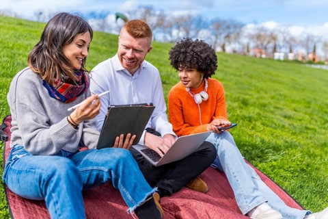 Three university students collaborating on a project, using a digital tablet and laptop while