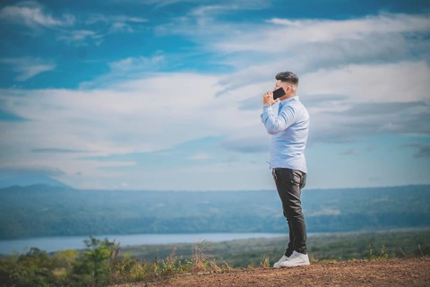 Handsome young man talking on the phone outdoors surrounded by nature. A person talking on the