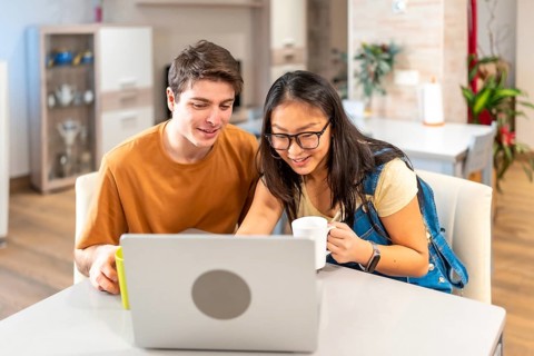 Multiethnic couple using laptop and drinking coffee at home, enjoying a relaxing moment together