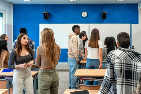 Diverse group of high school students interacting during break time, standing by desks in modern