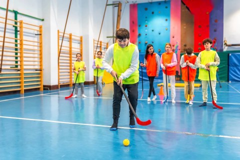 Group of preteen students wearing bibs, actively playing floorball during gym class in a lively