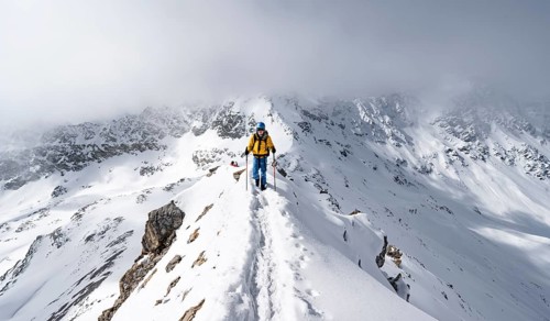 Mountaineer climbing up the narrow ridge of Piz Laviner, view of wintry mountain landscape, Grisons