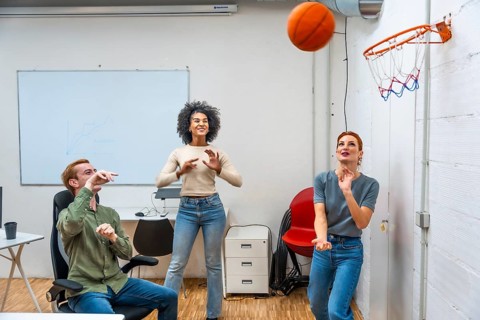 Diverse coworkers playing basketball in a meeting room of a modern office