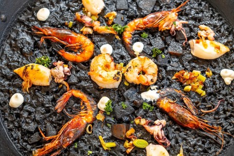 Close up of black rice paella with grilled shrimps, squid, and aioli, a typical dish from mallorca,