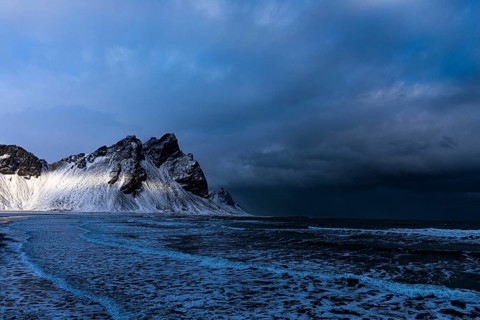 White foamy waves on the beach of Stokkness, behind snowy rocky slopes of Vestrahorn, near Höfn,
