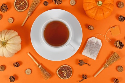 Cup of tea surrounded by seasonal fall decoration like pumpkins and orange slices on orange