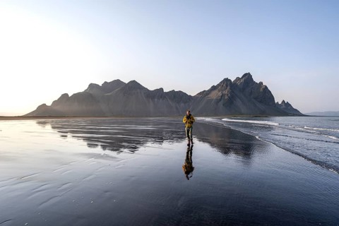 Tourist at black lava beach, sandy beach and sea, mountains Klifatindur reflected in the water,