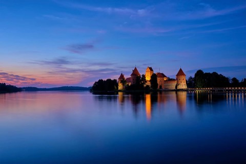 Trakai Island Castle in lake Galve illuminated in twilight reflecting in peaceful water, Lithuania,