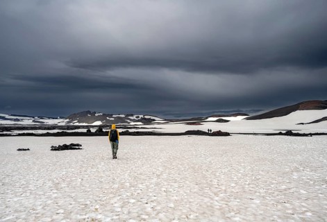 Hikers in snow-covered volcanic landscape with volcanic sand and petrified lava, crater of Askja
